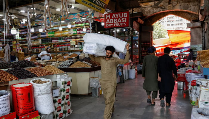 A man walks with sacks of supplies on his shoulder to deliver to a nearby shop at a market in Karachi on June 11, 2024. — Reueters