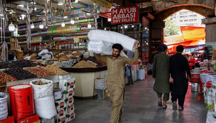 A man walks with sacks of supplies on his shoulder to deliver to a nearby shop at a market in Karachi on June 11, 2024. — Reuters