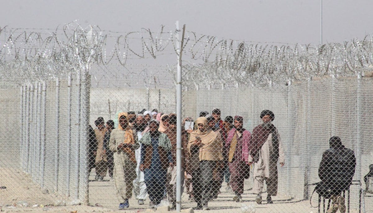 Pakistans and Afghans nationals walk along a fenced corridor as they enter Pakistan through the Pakistan-Afghanistan border crossing point in Chaman on February 27, 2022. — AFP