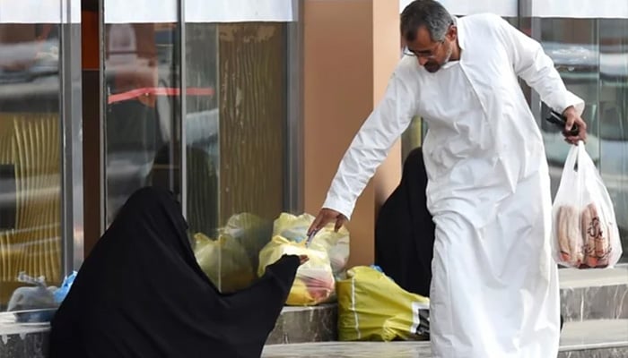 A Saudi man hands money to a woman begging outside a supermarket on a main street in Riyadh. — AFP/File