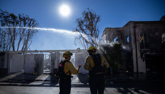 Firefighters stand on a road as water is sprayed over a property destroyed by the Palisades Fire, in Malibu, California, US, January 12, 2025. — Reuters