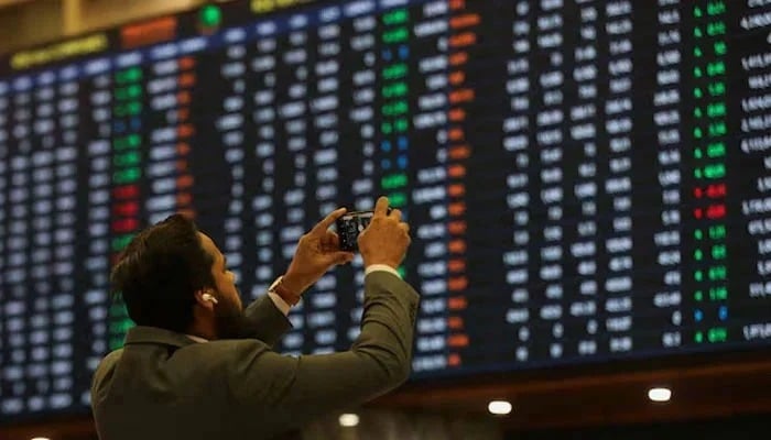 A man takes a photo of the electronic card on the Pakistan Stock Exchange in Karachi on November 28, 2023. - Reuters