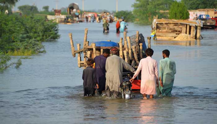 Men walk along a flooded road with their belongings, following rains and floods during the monsoon season in Sohbatpur, Pakistan August 28, 2022. — Reuters