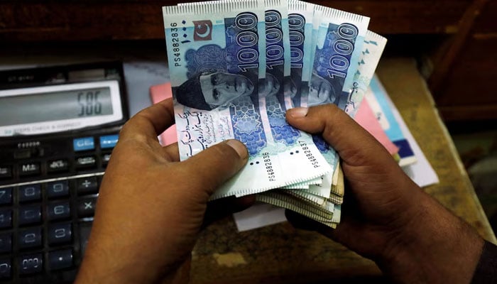 A trader counts Pakistani rupee notes at a currency exchange booth in Peshawar. — Reuters/File