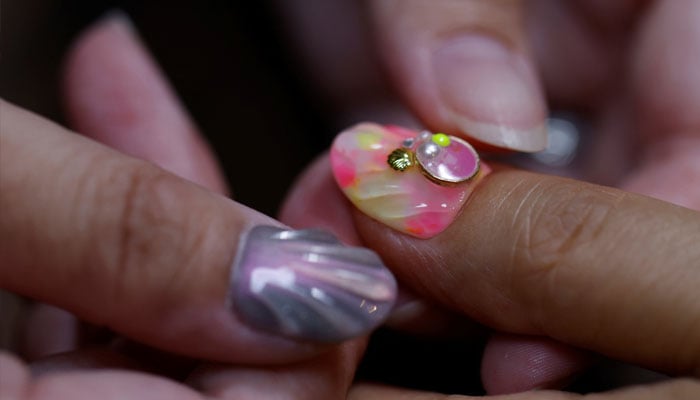 Japanese manicurist Naomi Arimoto presses a false nail with a decorative nail tip using plastic waste which she collected from the beach, onto a thumb of a customer at her nail salon in Chigasaki, Kanagawa Prefecture, Japan October 21, 2024. — Reuters