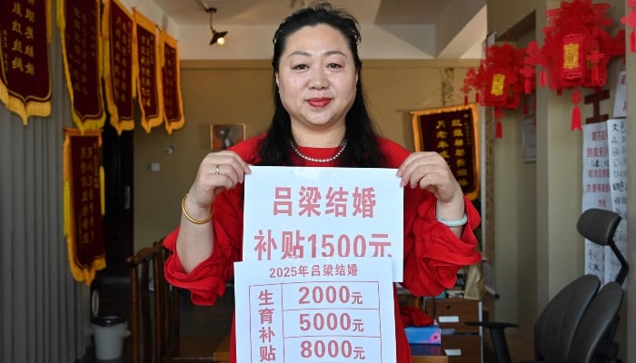 Matchmaker Feng Yuping holds poses with a poster featuring a government incentive of 1,500-yuan  for people to get married in Luliang, northern Chinas Shanxi province on February 10, 2025. — AFP