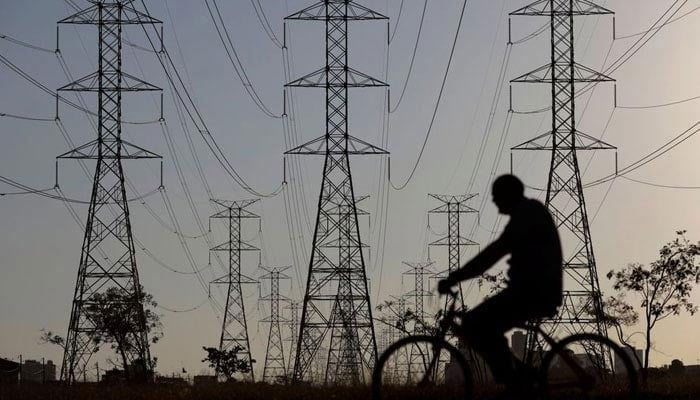 The representational image shows a man riding a bicycle near power lines connecting pylons of high-tension electricity. — Reuters/File