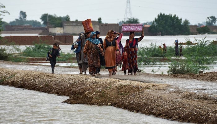 Women and children walk with their belongings towards a higher ground following rains and floods during the monsoon season in Dera Allah Yar, district Jafferabad, Balochistan on August 25, 2022. — Reuters