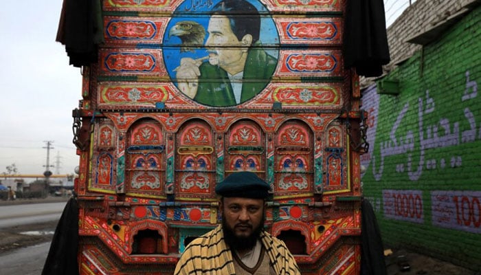 A supply truck owner  poses in front of his decorated supply truck with a portrait of Allama Iqbal at a workshop in Peshawar on January 29, 2024. — Reuters