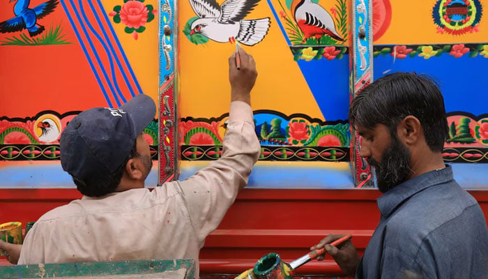 A truck art painter, paints an image of a dove on a supply truck as his colleague prepares colours at a workshop in Peshawar on November 27, 2023. — Reuters