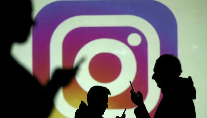 Silhouettes of mobile users are seen next to a screen projection of the Instagram logo in this picture illustration taken March 28, 2018. —Reuters