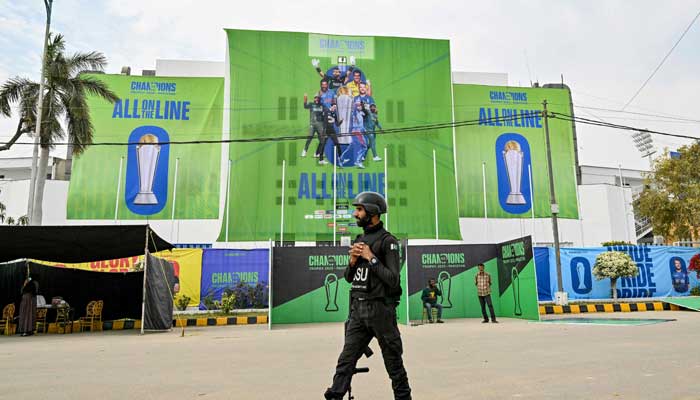 Pakistans police commando walks past posters displayed ahead of the Champions Trophy, outside the National Stadium in Karachi on February 17, 2025. — AFP