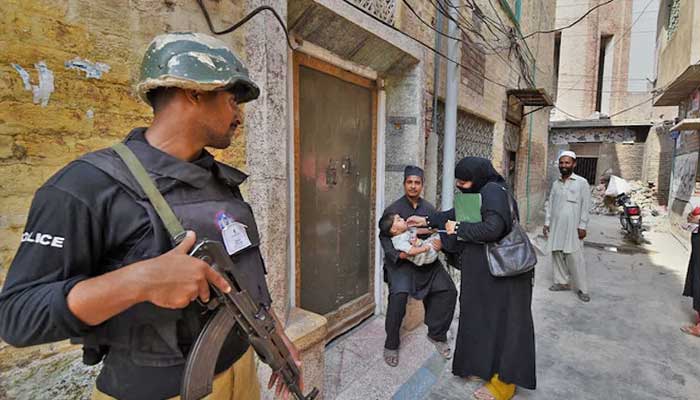 A Pakistani policeman is on the guard as a health worker administers polio falls to a child during a polio vaccination campaign in Peshawar, Pakistan, September 14, 2015. - AFP