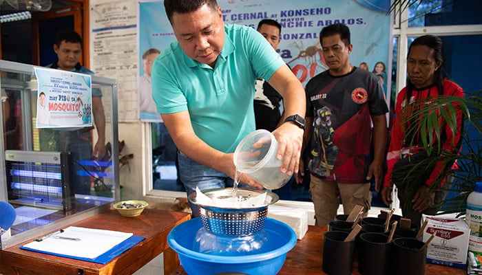 Village chief Carlito Cernal (C) pours a plastic container filled with water and mosquito larvaes handed over by residents into a strainer for counting at the start of peso for a mosquito programme to eradicate dengue in Manila on February 19, 2025. — AFP