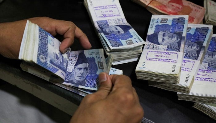 An employee counts Pakistani rupee notes at a bank in Peshawar. — Reuters/File