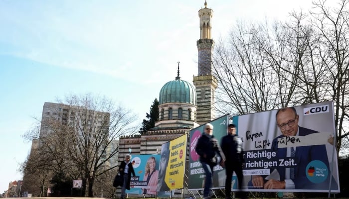 People walk past an election campaign poster of Friedrich Merz, Christian Democratic Union (CDU) party candidate for chancellor, the day before the parliamentary election, in Potsdam, Germany, February 22, 2025. — Reuters