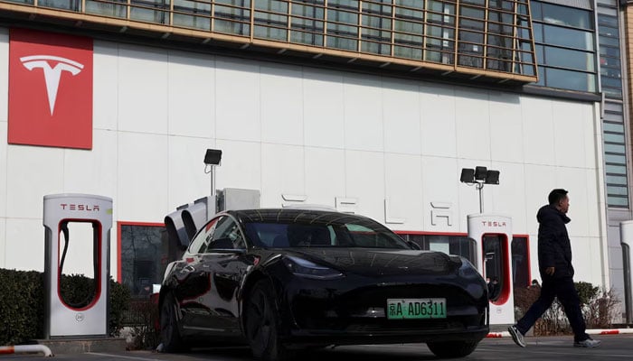 A man walks near a Tesla car at a charging station outside a store of the electric vehicle maker in Beijing, China on January 4, 2024. — Reuters