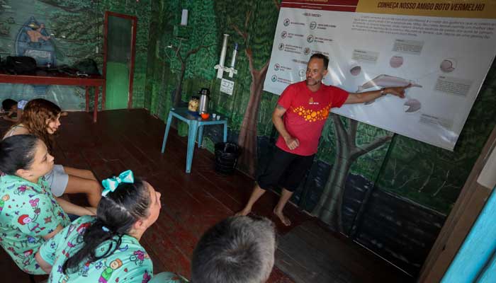 Physiotherapist Igor Simoes Andrade teaches on pink dolphins (Inia geoffrensis) to young people with disabilities before swimming with them on a floating boat on the Rio Negro river in Iranduba. — AFP