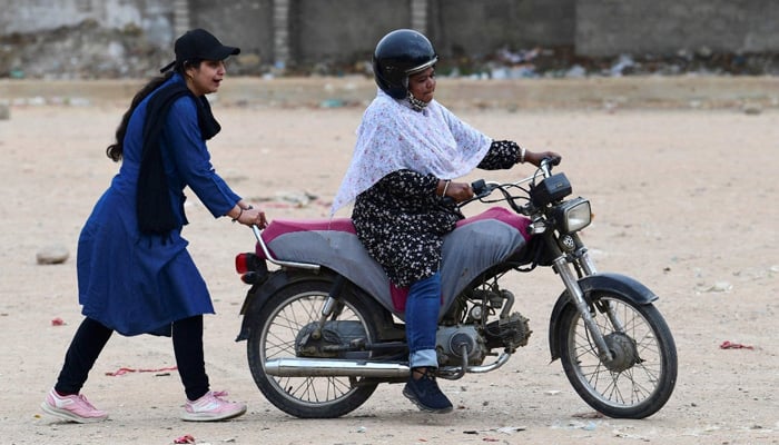 Zainab Safdar (L), an instructor with the women-only group Rowdy Riders, helps a student ride a motorbike during a riding lesson at an open ground in Karachi. — AFP/File