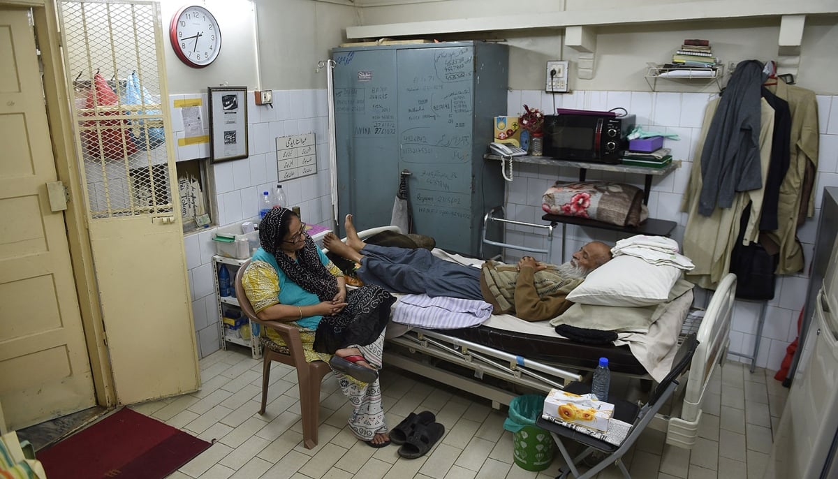 Abdul Sattar Edhi lies on a bed as his wife Bilquis Edhi is seated on a chair beside him in their Meethadar office in Karachi. — AFP/File