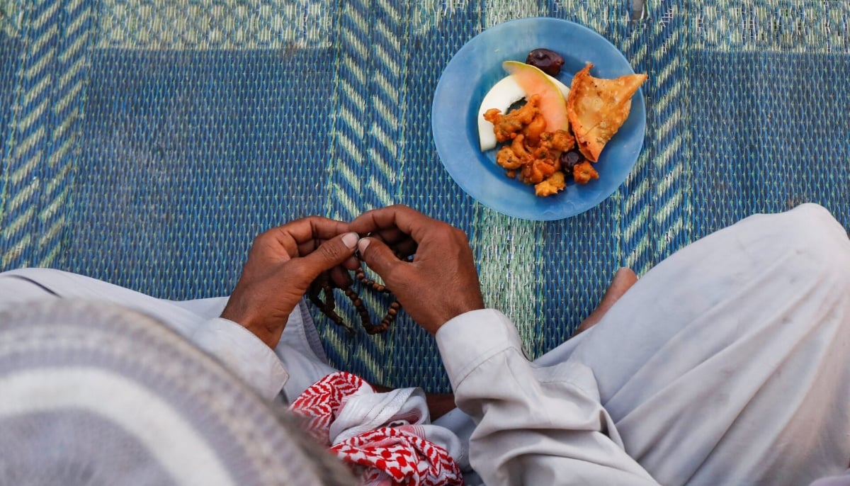 A man holds a tasbeeh, or prayer beads, as he sits with a plate of food before breaking fast during Ramadan, at a roadside in Karachi on March 28, 2023. — Reuters