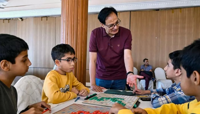 Pakistan Scrabble Association youth programme director Tariq Pervez gives direction to youngsters competing in a Scrabble championship organised in Karachi. — AFP