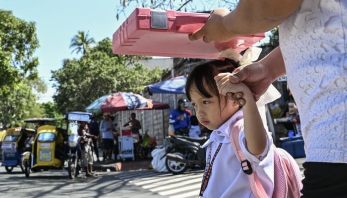 A man uses a school bag to protect a child from the sun as they leave school in Manila. — AFP/File