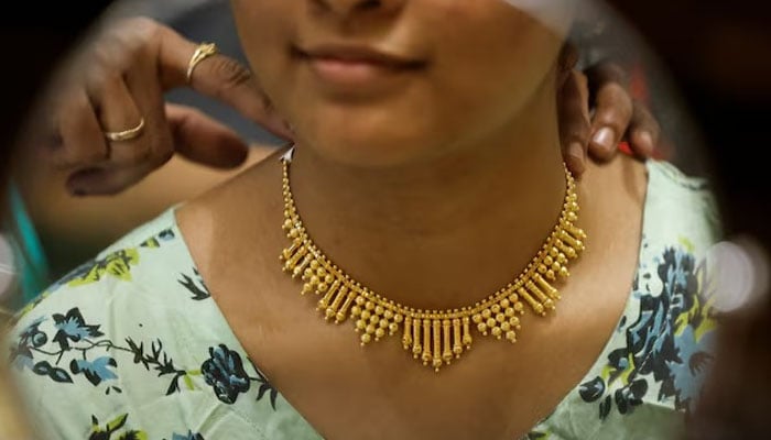 A woman tries a gold necklace in a jewelry exhibition hall during Dhanteras, a Hindu festival associated with Lakshmi, the goddess of wealth, in Mumbai, India, November 10, 2023.