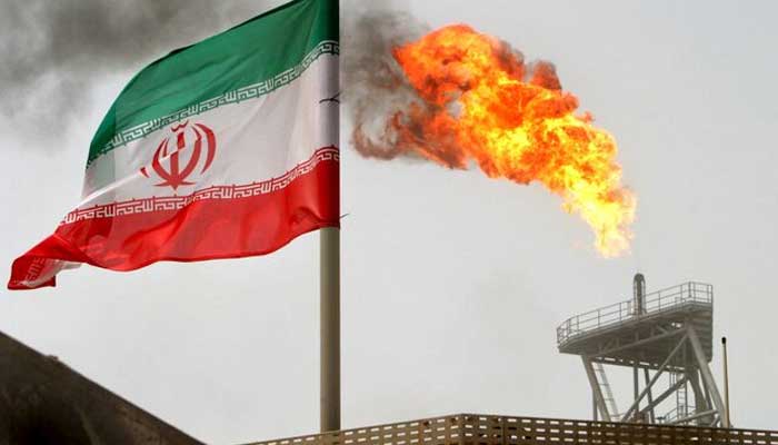 A gas flare on an oil production platform in the Soroush oil fields is seen alongside an Iranian flag in the Gulf July 25, 2005. — Reuters