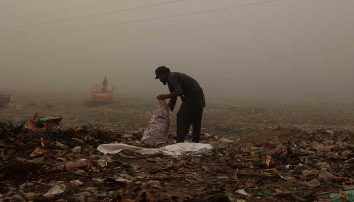 A ragpicker collects usable items from a dump yard on a smoggy morning in Peshawar, November 11, 2024. — Reuters