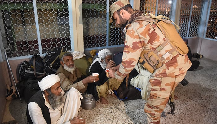 A soldier (right) hands out tea to freed train passengers gathered at the Mach railway station in Mach, Balochistan on March 11, 2025. — AFP