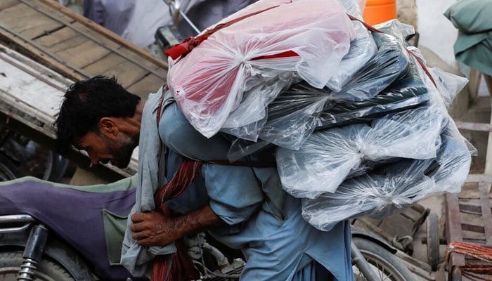 A labourer bends over as he carries packs of textile fabric on his back to deliver to a nearby shop in a market in Karachi on June 24, 2022. — Reuters