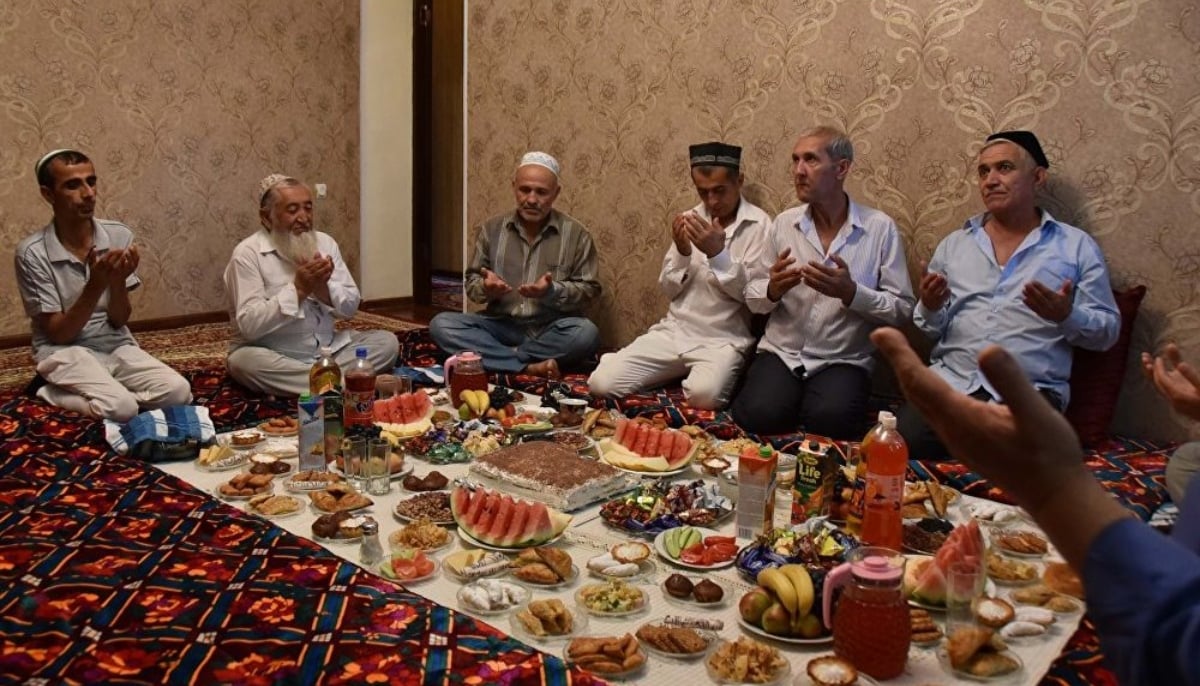 A group of men gathers around a traditional iftar feast, offering prayers before breaking their fast. —Asia Plus