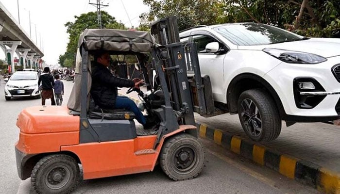 A traffic police official lifting a wrongly parked car with the help of a lifter at Murree Road, Rawalpindi. — APP/File