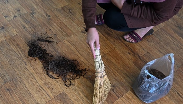 An Afghan woman hairdresser collecting hair left on the floor after giving a haircut to a client at a salon in Kabul on March 19, 2025. — AFP